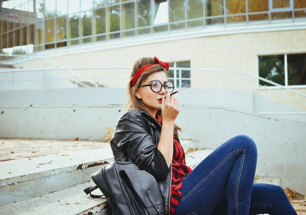 Wanita hipster muda berkacamata duduk di tangga dan merokok — Stok Foto