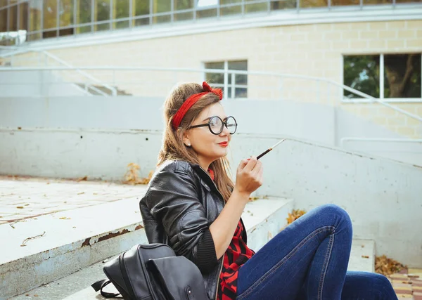 Young hipster woman in glasses sitting on stairs and smoking cigarette — Stock Photo, Image