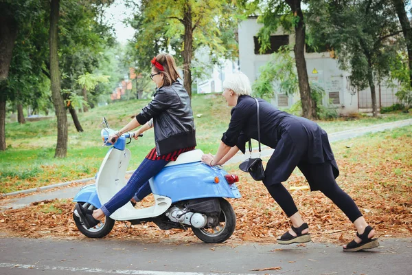İki genç kadın parkta vintage scooter ile biraz eğlenmek