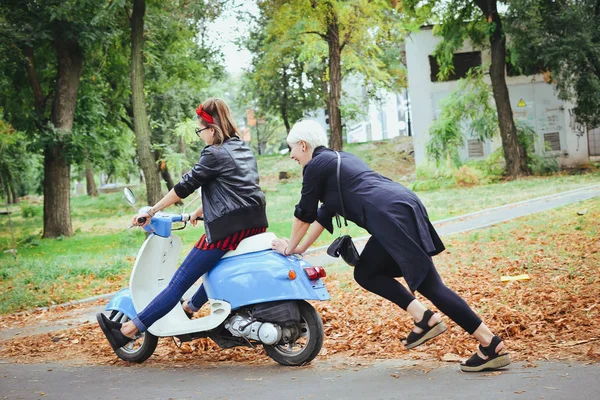 Duas jovens mulheres se divertindo com scooter vintage no parque — Fotografia de Stock