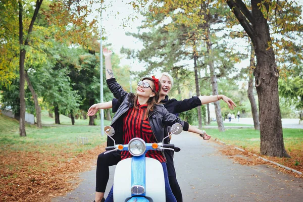 Duas jovens mulheres se divertindo com scooter vintage no parque — Fotografia de Stock