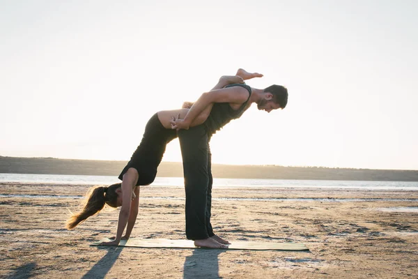 Man and Woman in Black Sport Clothes Doing Acroyoga on a Sea Beach