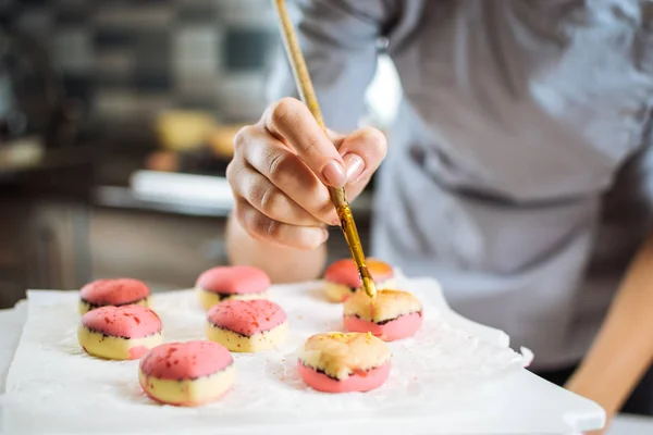 O confeiteiro decorar com escova os bolos nas formas de corações — Fotografia de Stock