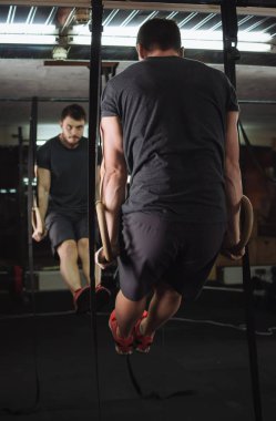 Spor süspansiyon halkaları üzerinde yapan genç ve güzel erkek çeker