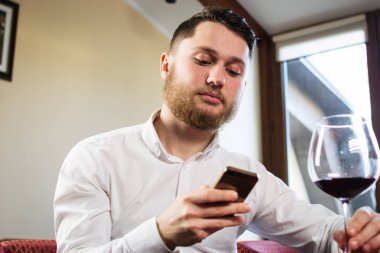 Telefon ve alarak kadeh şarap restoranda kullanan genç çekici adam
