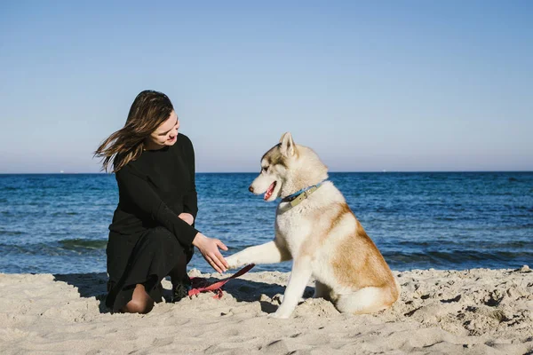 Mulher na praia do mar com cão husky siberiano — Fotografia de Stock