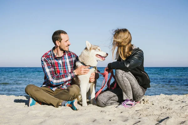 Casal na praia com cão husky siberiano — Fotografia de Stock