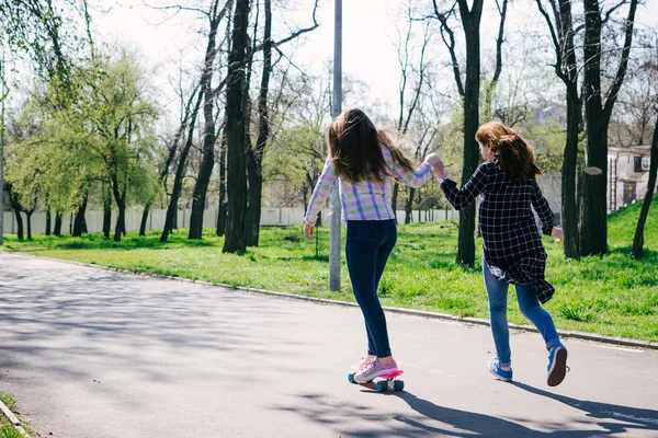 Positive sister girls running, skateboarding and having fun together in park — Stock Photo, Image
