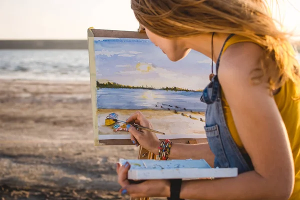 Young woman artist painting landscape in the open air on the beach — Stock Photo, Image