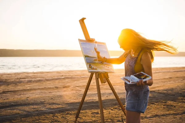 Young woman artist painting landscape in the open air on the beach