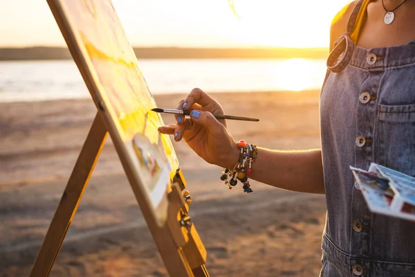 Young woman artist painting landscape in the open air on the beach, close up