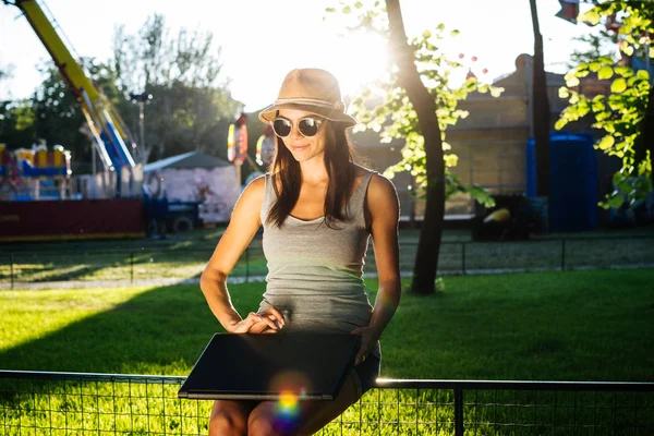 Beautiful young woman in hat using laptop in park