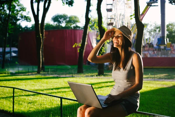 Веселая молодая женщина в шляпе с ноутбуком в парке — стоковое фото