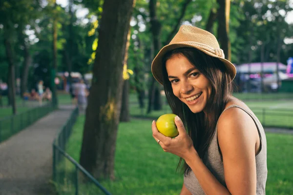 Портрет молодої чарівної брюнетки, що їсть зелене яблуко в парку — стокове фото