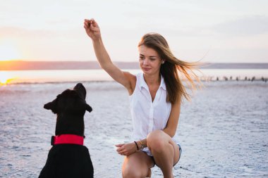 Genç kadın eğitim labrador retriever köpek gün batımında sahilde
