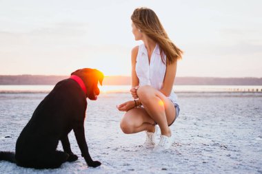 Genç kadın, labrador retriever köpek gün batımında sahilde