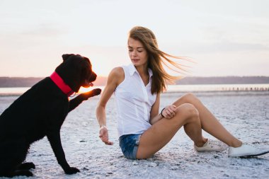 Genç kadın eğitim labrador retriever köpek gün batımında sahilde