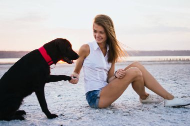 Genç kadın eğitim labrador retriever köpek gün batımında sahilde