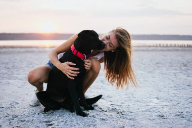Mutlu genç kadın, labrador retriever köpek gün batımında sahilde