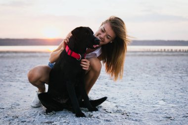 Mutlu genç kadın, labrador retriever köpek gün batımında sahilde