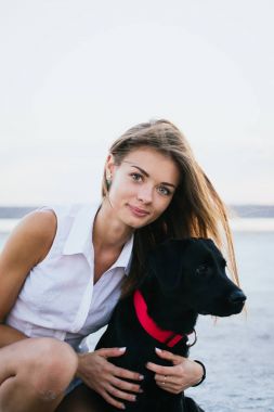 Mutlu genç kadın, labrador retriever köpek gün batımında sahilde