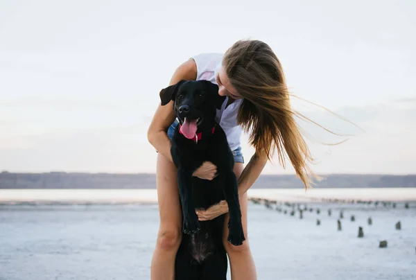 Mladá žena objímala s pes labrador retriever na pláži při západu slunce — Stock fotografie