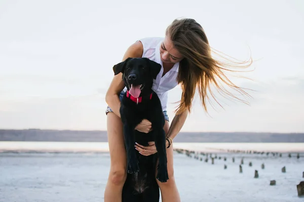 Jovem abraço feminino com cão labrador retriever na praia ao pôr do sol — Fotografia de Stock