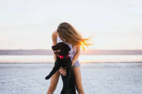 Jovem abraço feminino com cão labrador retriever na praia ao pôr do sol — Fotografia de Stock