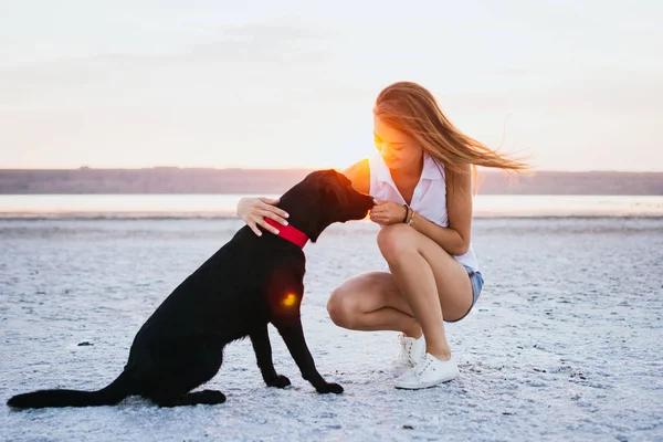 Genç kadın eğitim labrador retriever köpek gün batımında sahilde