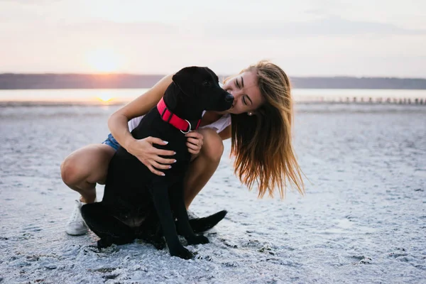 Mutlu genç kadın, labrador retriever köpek gün batımında sahilde