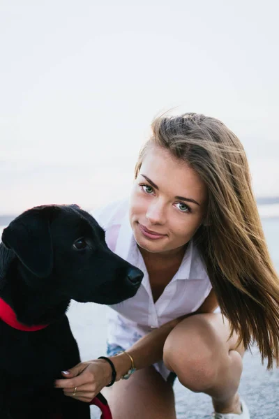 Jovem fêmea feliz com cão labrador retriever na praia ao pôr do sol — Fotografia de Stock