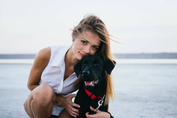 Feliz hembra joven con perro labrador retriever en la playa al atardecer — Foto de Stock