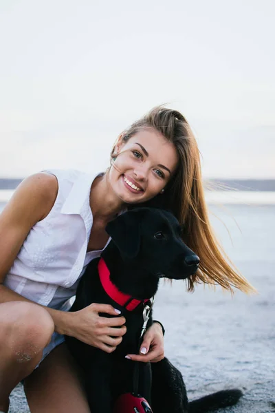 Jovem fêmea feliz com cão labrador retriever na praia ao pôr do sol — Fotografia de Stock