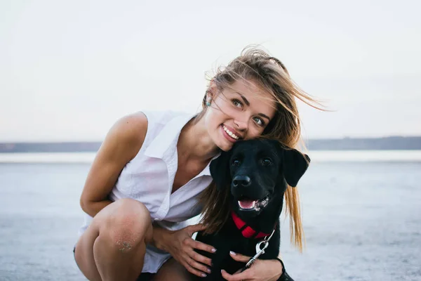 Mutlu genç kadın, labrador retriever köpek gün batımında sahilde