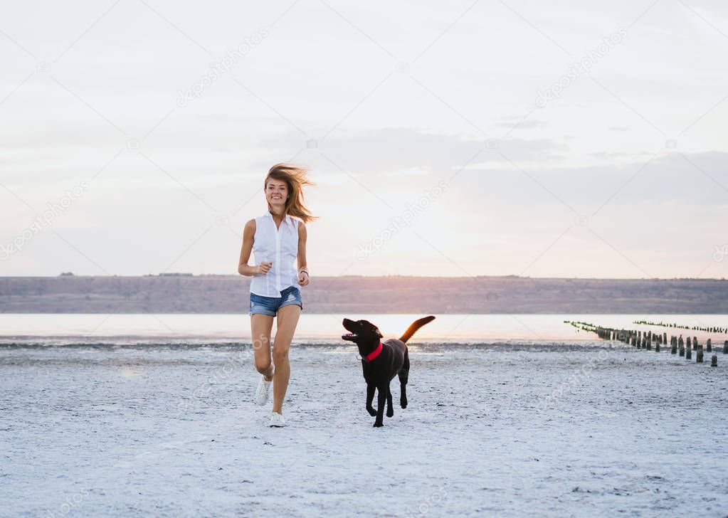 Young female walking with labrador retriever dog on the beach at sunset