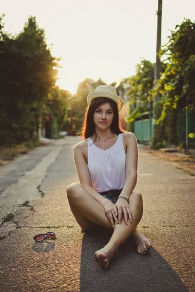 Молода жінка в капелюсі сидить на дорозі в сільській місцевості — стокове фото