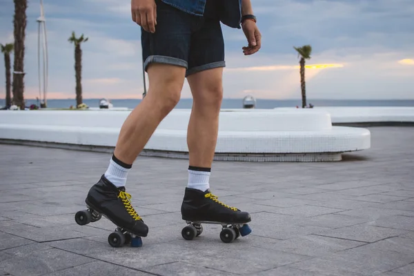 Joven hombre caucásico patinaje sobre ruedas con patines quad cerca del mar, de cerca —  Fotos de Stock