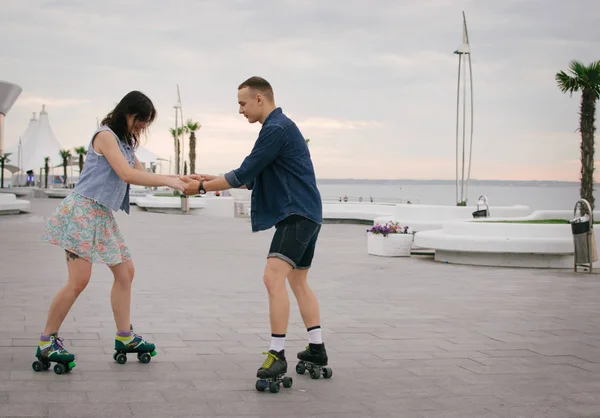Bonito casal doce montando em patins patins quads de mãos dadas perto do mar — Fotografia de Stock