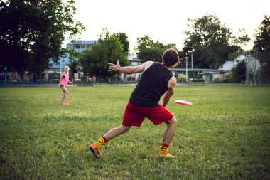 Genç adam ve günbatımı sırasında parkta frizbi oynayan kadın