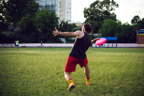 Jovem jogando frisbee no parque durante o pôr do sol — Fotografia de Stock