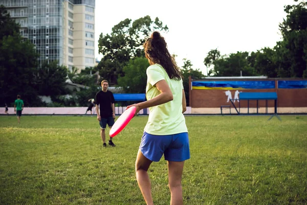 Jovem mulher e homem jogando frisbee no parque durante o pôr do sol — Fotografia de Stock