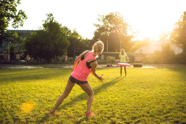 Twee jonge en mooie vrouwen spelen frisbee in het park — Stockfoto
