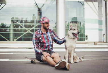 Sibirya husky köpek sokak yolda ile kaykay üzerinde oturan genç hipster adam