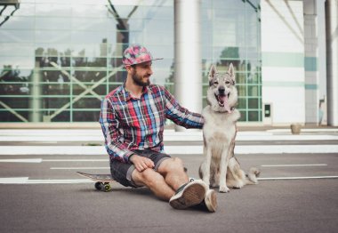 Sibirya husky köpek sokak yolda ile kaykay üzerinde oturan genç hipster adam