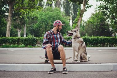 Sibirya husky köpek sokak yolda ile kaykay üzerinde oturan genç hipster adam