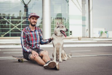 Sibirya husky köpek sokak yolda ile kaykay üzerinde oturan genç hipster adam