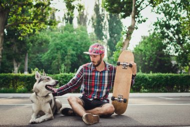 Sibirya husky köpek sokak yolda ile kaykay üzerinde oturan genç hipster adam