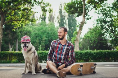 Kaykay ile komik Sibirya husky köpek şapkalı üzerinde oturan genç hipster adam 