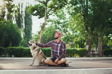 Sibirya husky köpek sokak yolda ile kaykay üzerinde oturan genç hipster adam