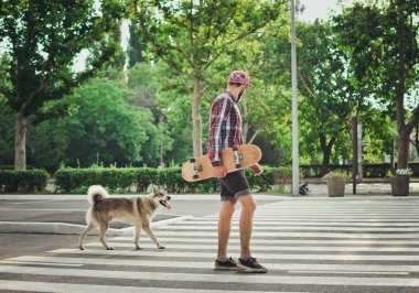 Genç adam kaykay ve Sibirya husky köpek ile sokak yolda yürürken